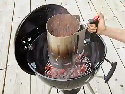 Eine Person hält einen Anzündkamin über einen Grill auf einer Holzterrasse.