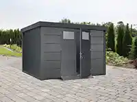 Ein graues Gartenhaus steht offen auf einem gepflasterten Platz, umgeben von Sträuchern.