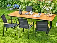 Ein Tisch mit Geschirr steht auf einem Rasen, umgeben von vier Stühlen und blühenden Büschen.