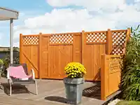 Ein Holzsichtschutzzaun steht auf einer Terrasse, daneben ein Stuhl und ein Blumentopf.