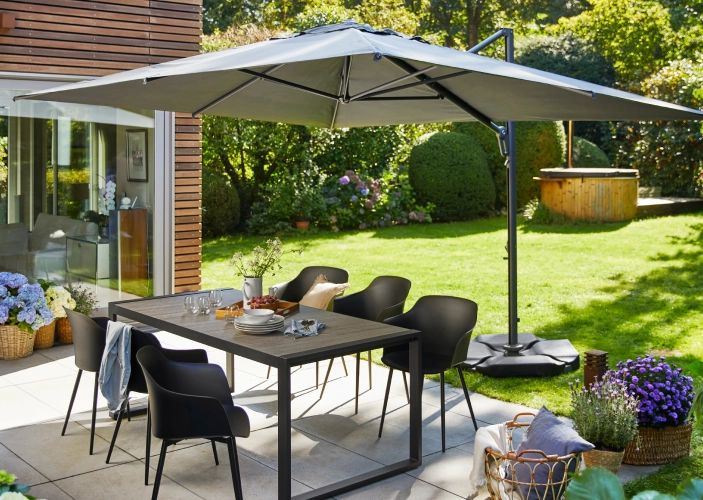 Grauer Sonnenschirm spendet einer Sitzgruppe in einem Garten schatten
