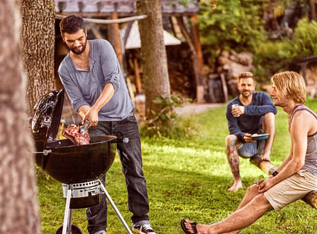Ein Mann der gerade fleisch grillt und sich dabei mit zwei Männern unterhält