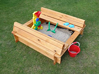 Eine Holzsandkiste mit Spielzeug steht auf einer grünen Rasenfläche.