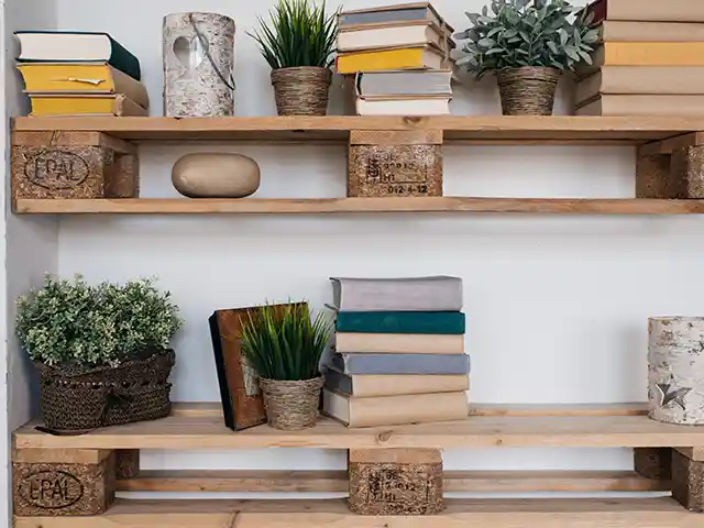Bücher und Pflanzen stehen auf einem rustikalen Holzregal vor einer weißen Wand.