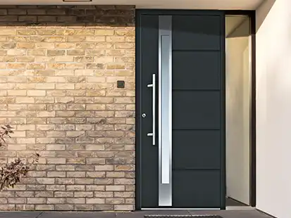 Eine schwarze Haustür mit Glasstreifen, eingebaut in eine Ziegelsteinmauer.