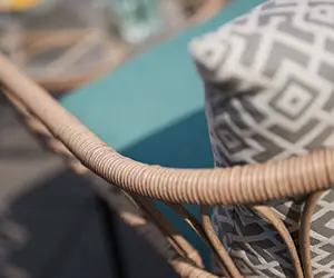 Ein gemustertes Kissen liegt auf einem Stuhl mit Rattangeflecht im Freien.