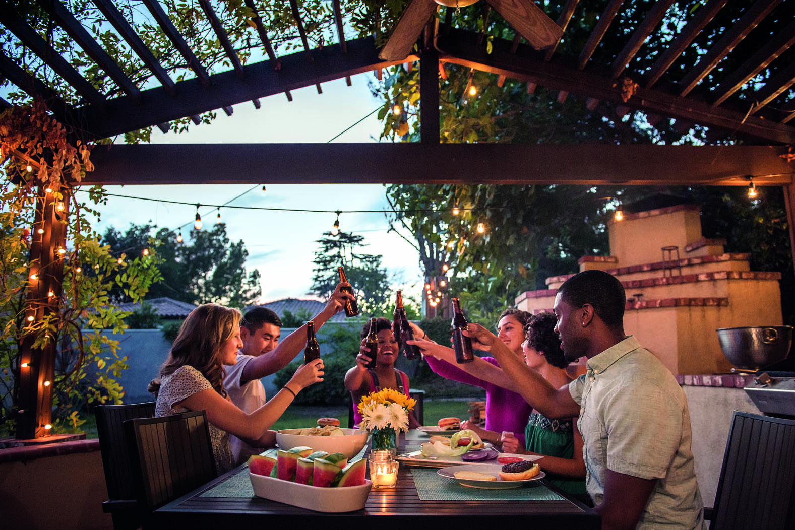 Eine Gartenparty mit Freunden die an einem Gartentisch zusammen sitzen essen und trinken 