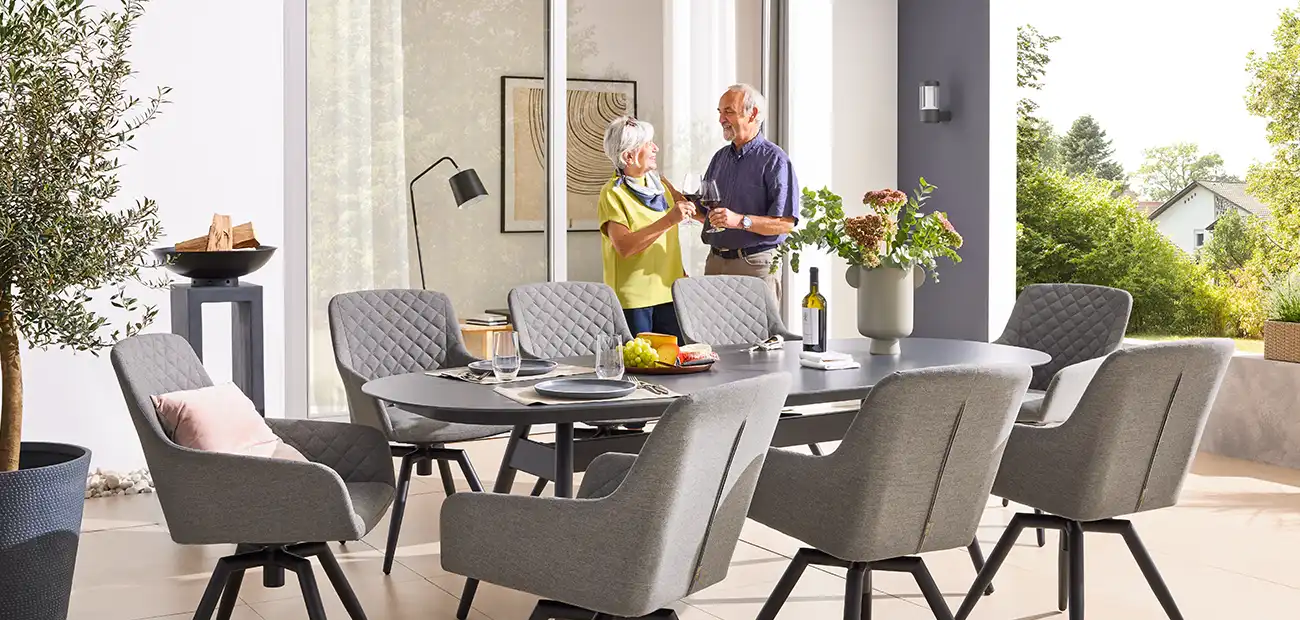 Ein älteres Paar trinkt Wein in einem stilvollen, modernen Esszimmer mit grauen Stühlen.