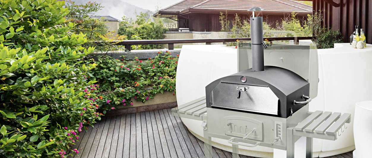 Ein Holzkohlegrill mit einem Pizzaofen Aufsatz auf der Holzterrasse