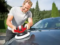 Ein Mann poliert ein Auto mit einem roten Polierer in einer grünen Umgebung.